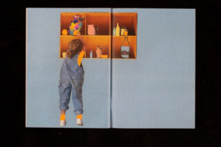 Ein Kind im blauen Overall steht auf Zehenspitzen und greift nach einem Gegenstand auf einem hohen Holzregal, das mit verschiedenen Flaschen und Gläsern vor einem hellblauen Hintergrund gefüllt ist.