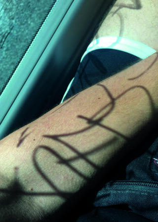 Sonnenlicht wirft den Schatten eines Fensterrahmens und seines Gittermusters auf den Arm einer Person, die in der Nähe eines Autofensters ruht.