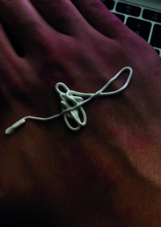 Ein verwickeltes weißes Ohrhörerkabel liegt auf dem Handrücken einer Person in der Nähe einer Laptoptastatur.