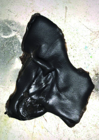 Ein Stück glänzendes schwarzes Material mit faltiger Textur liegt flach auf einer gesprenkelten, hellen Oberfläche.