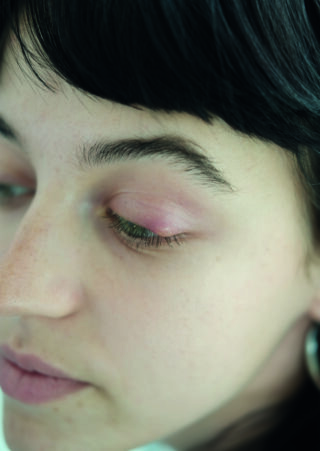 Nahaufnahme des Gesichts einer Person mit geschlossenen Augen, die die natürliche Hautstruktur, rosa Augenlider und dunkles Haar zeigt.