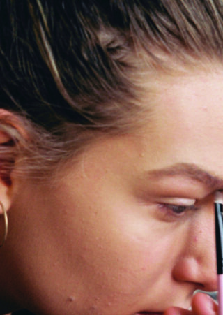 Eine Person mit heller Haut und geflochtenem Haar verwendet einen Augenbrauenstift, um ihre Augenbrauen auszufüllen.