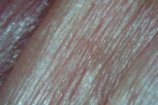 Nahaufnahme der menschlichen Haut, die feine Linien, Fältchen und eine natürliche Textur in rosa Tönen zeigt.