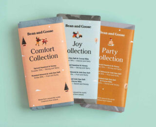 Drei Schokoriegel von Bean and Goose – Comfort Collection, Joy Collection und Party Collection – sind nebeneinander auf einer hellgrünen Oberfläche angeordnet.