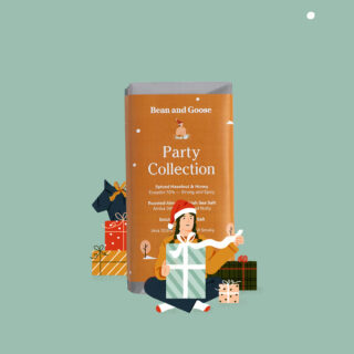 Eine Person sitzt im Schneidersitz und hält ein großes Geschenk, umgeben von verpackten Geschenken, vor einem Schokoriegel der Bean and Goose Party Collection auf grünem Hintergrund.