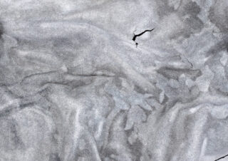 Nahaufnahme einer strukturierten, grauen, faltigen Oberfläche mit einem sichtbaren Riss, der sich über den oberen rechten Bereich erstreckt.