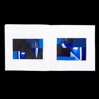 Ein offenes Buch zeigt auf beiden Seiten abstrakte geometrische Collagenkunst in Blau und Schwarz vor einem schlichten schwarzen Hintergrund.