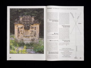 Aufgeschlagenes Magazin mit einem Foto eines verwitterten Steindenkmals im Freien auf der linken Seite und deutschem Text mit Diagrammen auf der rechten Seite.