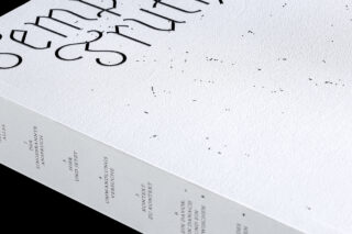 Nahaufnahme eines weißen Buchumschlags und Buchrückens mit minimalistischem schwarzem Text in deutscher Sprache mit vereinzelten dekorativen Punkten und einer strukturierten Oberfläche.