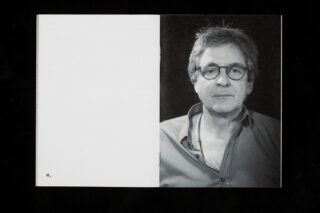 Eine Broschüre ist geöffnet. Sie zeigt eine leere linke Seite mit dem Buchstaben „M.“ unten und ein Schwarzweißporträt einer Person mittleren Alters mit Brille auf der rechten Seite.