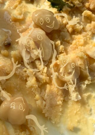 Nahaufnahme eines krümeligen, gelblichen Lebensmittels mit Trauben obenauf, überlagert mit skurrilen, durchscheinenden Cartoon-Gesichtern und -Armen, die auf die Trauben gezeichnet sind.