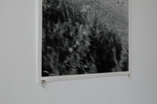 Ein Schwarzweißfoto mit unscharfer Textur ist mit zwei Büroklammern an den unteren Ecken an einer weißen Wand befestigt.