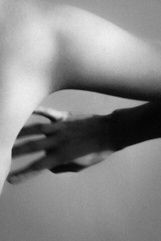 Nahaufnahme eines Schwarzweißfotos der Schulter einer Person mit dem Schatten einer Hand auf ihrer Haut.