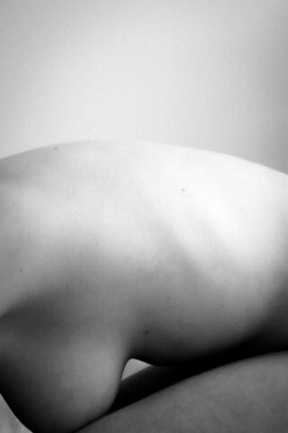 Schwarzweißfoto des nackten Rückens und der Schultern einer Person mit minimalistischer Beleuchtung und einem sanften Farbverlaufshintergrund.