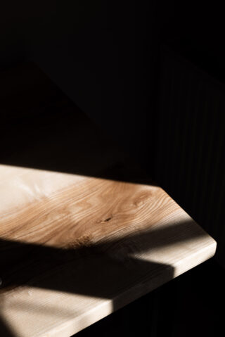 Eine Holztischplatte wird teilweise vom Sonnenlicht beleuchtet, wodurch scharfe Schatten und kontrastierendes Licht auf der Oberfläche entstehen.