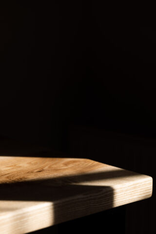 Eine Holztischplatte wird teilweise vom Sonnenlicht beleuchtet, der Rest der Szene liegt im tiefen Schatten.