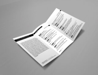 Auf einer grauen Fläche liegt eine gefaltete schwarzweiße Broschüre auf, die Text in Spalten mit Abschnittsüberschriften und fettgedruckten Wörtern anzeigt.