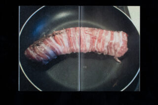 Ein Stück mit Speck umwickeltes Fleisch wird in einer schwarzen Bratpfanne auf einem Herd gebraten.