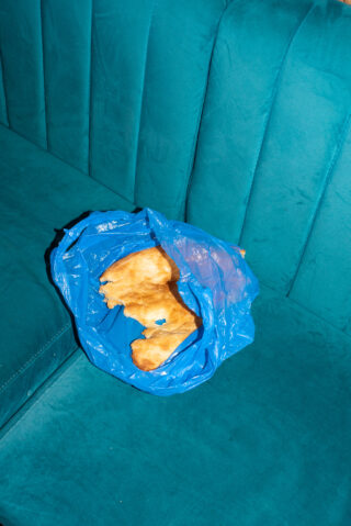 Ein Stück Fladenbrot in einer blauen Plastiktüte liegt auf einem blaugrünen Polstersofa.