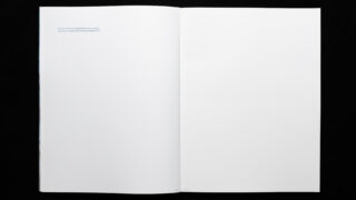 Ein offenes Buch auf einer schwarzen Oberfläche, das größtenteils leere weiße Seiten mit einer kurzen Zeile kleinen Textes oben links auf der linken Seite zeigt.