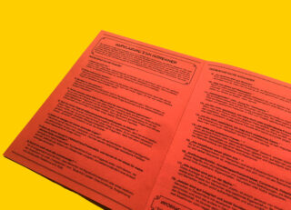 Eine orangefarbene Broschüre mit deutschem Text auf gelbem Hintergrund wird geöffnet. Die Überschriften und mehrere Abschnitte mit Informationen sind sichtbar.