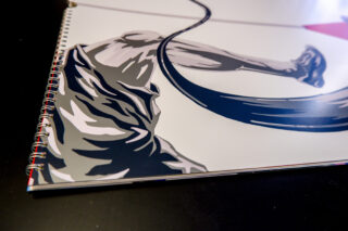 Abbildung der Beine einer Person, die Seil springt, auf einem Spiralnotizbuch, mit Fokus auf dem Seil und den Shorts in Graustufen und Marinetönen.