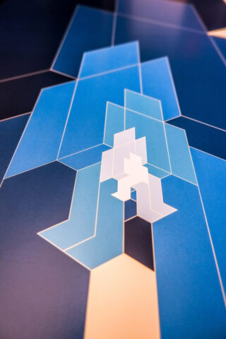 Abstraktes geometrisches Muster mit überlappenden blauen und weißen Formen mit scharfen Winkeln und kräftigen Linien auf dunklem Hintergrund.