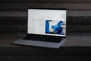 Auf Betonstufen steht ein Laptop, auf dem eine Webseite mit Text, ein Foto von behandschuhten Händen, die mit Lebensmitteln hantieren, und ein vertikales Balkendiagramm angezeigt werden.