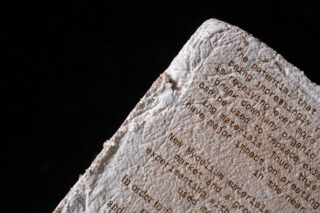 Eine Nahaufnahme einer strukturierten, rauen Oberfläche mit teilweise sichtbarem getipptem Text, fotografiert vor einem schwarzen Hintergrund.