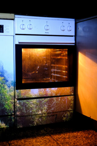 Ein weißer Backofen mit beleuchtetem Innenraum ist in einen Küchenschrank eingebaut. Die Backofentür ist geschlossen, der umliegende Bereich ist schwach beleuchtet.