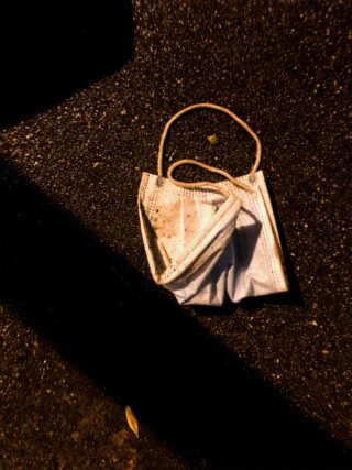 Eine weggeworfene blaue Gesichtsmaske liegt zerknittert auf einer dunklen, nassen Asphaltoberfläche.