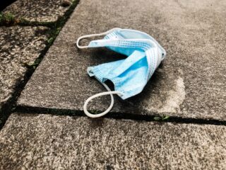 Eine weggeworfene blaue OP-Gesichtsmaske liegt auf einem Betonpflaster.
