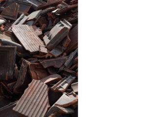 Ein Haufen zerbrochener, rotbrauner Welldachziegel, dicht an dicht gestapelt.