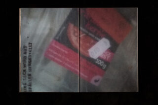 Ein verschwommenes Bild eines verpackten Lebensmittels mit einem sichtbaren Preisaufkleber und teilweise lesbarem deutschen Text an der Seite.