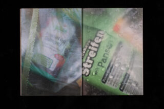 Nahaufnahme einer Produktverpackung mit deutschem Text, teilweise verdeckt durch eine grüne Plastiktüte und Kondenswasser oder Wassertropfen auf der Oberfläche.