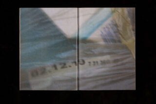 Ein verschwommenes Bild zeigt eine Nahaufnahme einer Oberfläche mit den Zahlen „12.12.19 731390“, die teilweise durch ein durchscheinendes Material sichtbar sind.