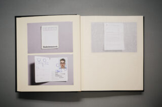 Ein aufgeschlagenes Buch zeigt auf der linken Seite zwei Ausweisdokumente, eines mit einem Lichtbildausweis und auf der rechten Seite ein unscharfes Dokument.