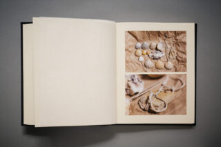 Ein offenes Buch mit zwei auf braunem Papier angeordneten Fotos von Muscheln und kleinen Naturobjekten und einer leeren Seite auf der linken Seite.