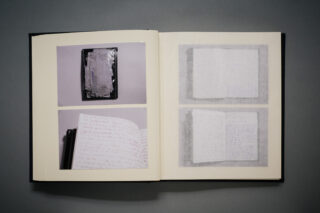 In einem offenen Buch sind vier Fotos zu sehen: eines von einem Stapel Papier, eines mit handgeschriebenem Text und zwei Bilder von offenen Notizbüchern mit verschwommener Schrift.