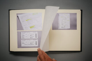 Eine Hand blättert in einem Fotoalbum, das Bilder von Dokumenten, Unterlagen und Bordkarten auf hellem Hintergrund zeigt.