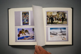 Eine Hand blättert in einem Fotoalbum, das vier Bilder zeigt, darunter ein Gemälde, eine Menschenmenge mit Schafen, ein Kunstwerk mit Figuren und ein Flugzeug auf einer sandigen Landebahn.