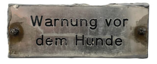 Ein Metallschild mit der deutschen Aufschrift „Warnung vor dem Hund“.