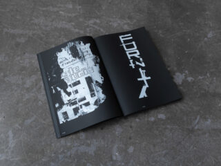 Auf einer Betonoberfläche liegt ein offenes Buch, das auf zwei Seiten abstrakte schwarz-weiße Grafiken und fetten, verzerrten Text zeigt.