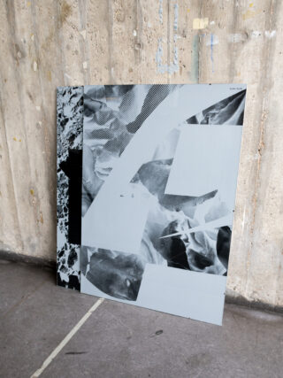 Ein großes abstraktes Schwarz-Weiß-Kunstwerk mit geometrischen und strukturierten Mustern lehnt an einer rauen Betonwand auf einem grauen Boden.