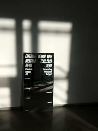 An einer weißen Wand steht ein Poster mit Veranstaltungsdetails, das durch Jalousien vom Sonnenlicht beleuchtet wird und Schatten auf Boden und Wand wirft.