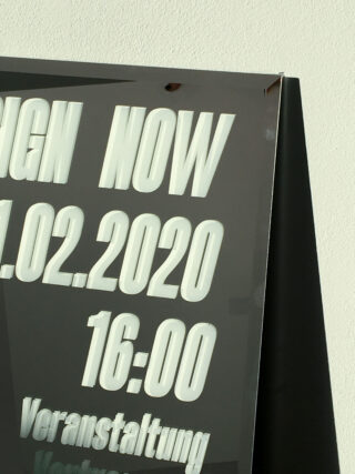 Auf einem reflektierenden Schild sind das Datum 21.02.2020 und die Uhrzeit 16:00 Uhr sowie die Worte „JETZT UNTERSCHREIBEN“ und der deutsche Text „Veranstaltung“ teilweise sichtbar.