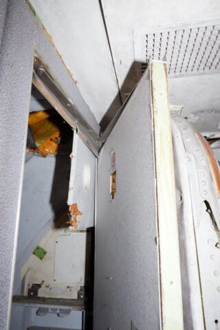 Eine beschädigte und teilweise kaputte Tür mit freiliegender Isolierung und Innenverkleidung in einer Flugzeugkabine.