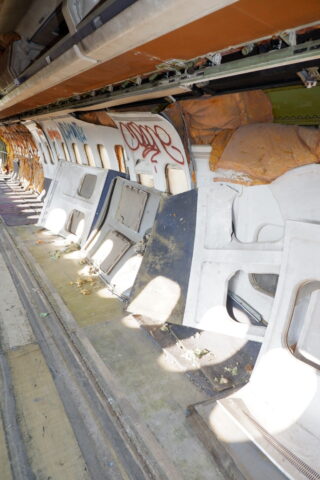 Innenraum eines verlassenen Flugzeugs mit fehlenden Sitzen, freiliegender Isolierung, Graffiti an den Wänden und verstreutem Schutt auf dem Boden.