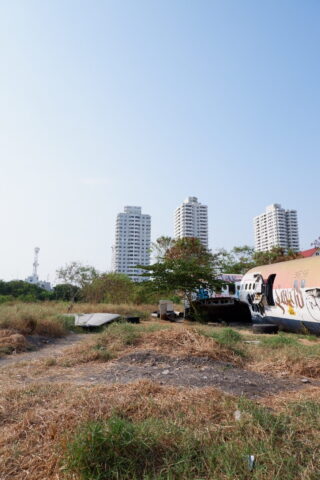 Im Hintergrund stehen drei Hochhäuser hinter einer Wiese mit verstreutem Schutt und einer mit Graffiti besprühten Struktur im Vordergrund.