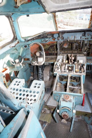 Cockpit eines alten, außer Dienst gestellten Flugzeugs mit abgenutzten Sitzen, Steuerhörnern, Instrumententafeln und verschiedenen Hebeln.